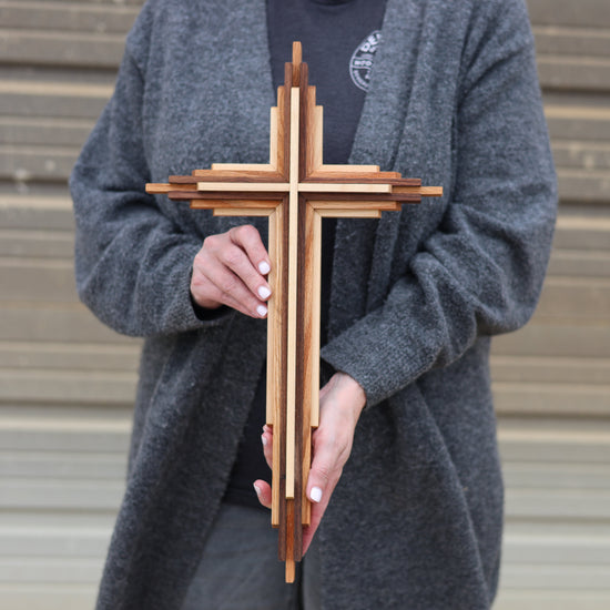 Person holding a wooden cross against a neutral background
